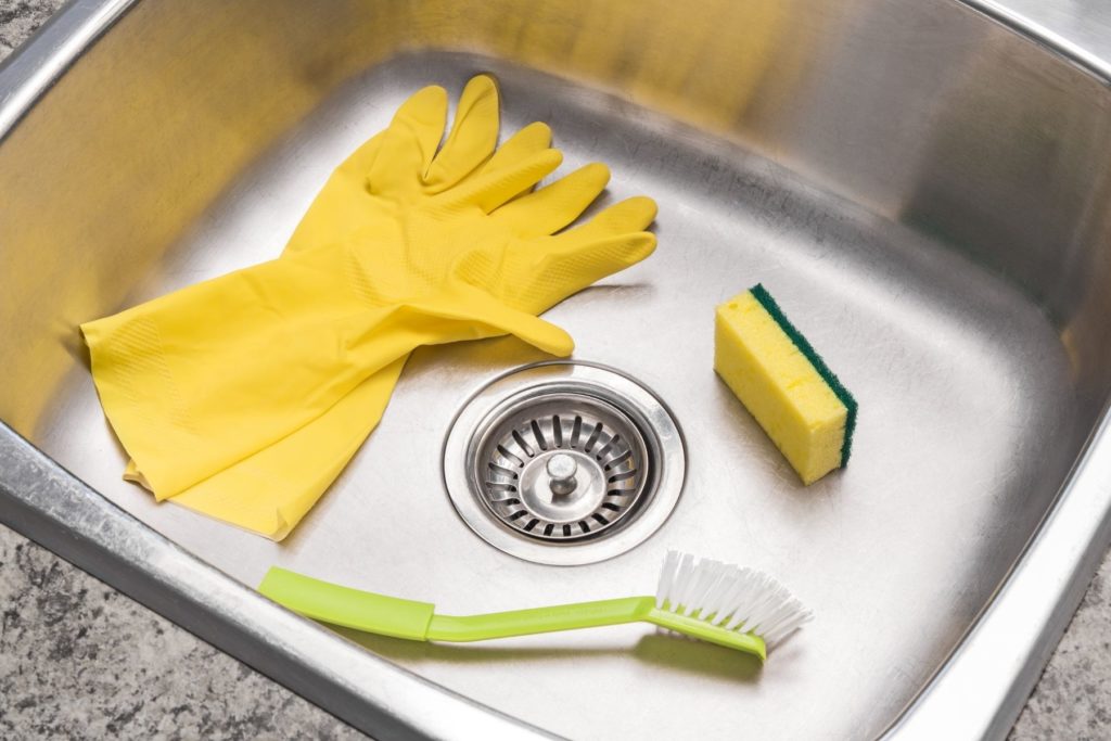 Gloves, sponge and brush in a clean kitchen sink